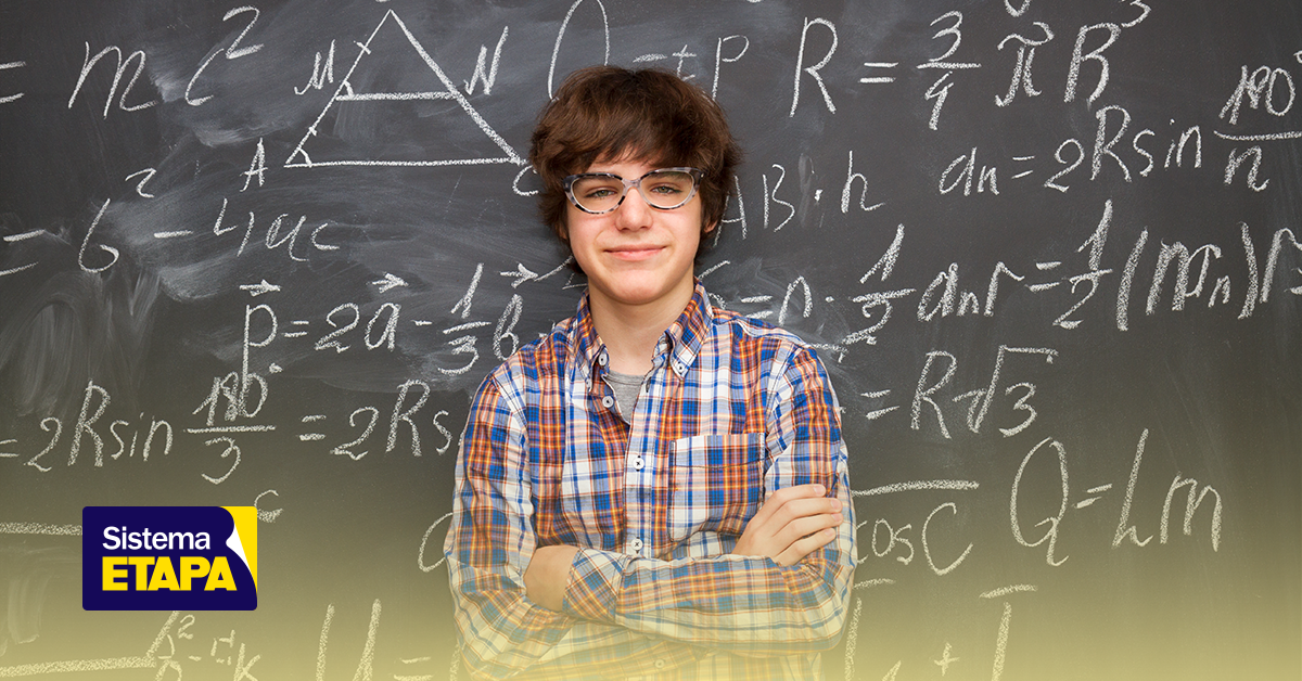 Jovem estudante feliz na sala de aula com quadro de fórmulas matemáticas relacionadas à IPhO - Olimpíada Internacional de Física ao fundo.
