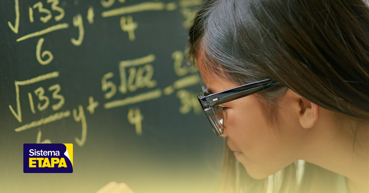 Estudante de colégio se preparando para o ENEM, focada na prova de Matemática, resolvendo questões ao lado de um quadro com problemas matemáticos escritos à giz.